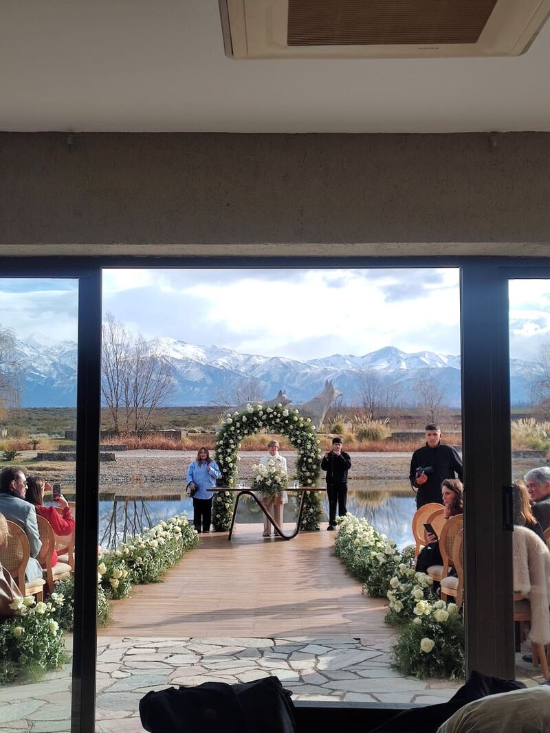 Arco de flores da cerimônia com o casal e a Cordilheira dos Andes emoldurados pela janela
